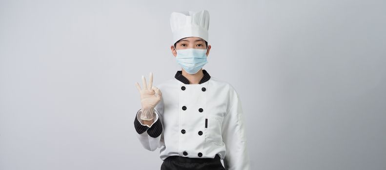 Asian woman chef in white color uniform with hygienic such as medical face mask and rubber hand glove for prevent or protect covid-19 or coronavirus pandemic. Studio shot and copy space.