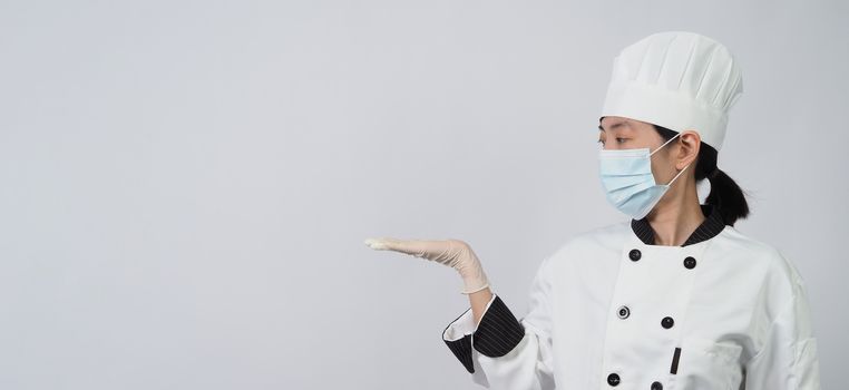 Asian woman chef in white color uniform with hygienic such as medical face mask and rubber hand glove for prevent or protect covid-19 or coronavirus pandemic. Studio shot and copy space.