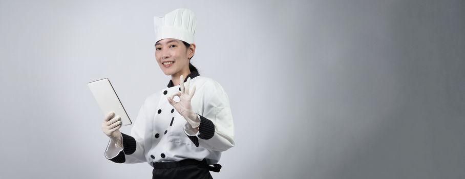 Middle aged of asian woman chef holding smartphone or digital tablet and received order from online shop or merchant application. she smiling in chef uniform and standing in studio with white color background.