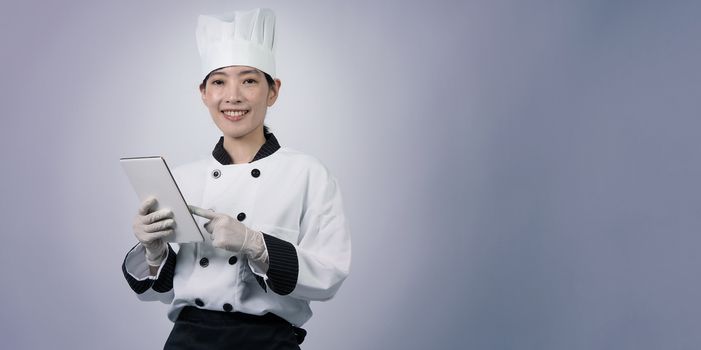 Middle aged of asian woman chef holding smartphone or digital tablet and received order from online shop or merchant application. she smiling in chef uniform and standing in studio with white color background.