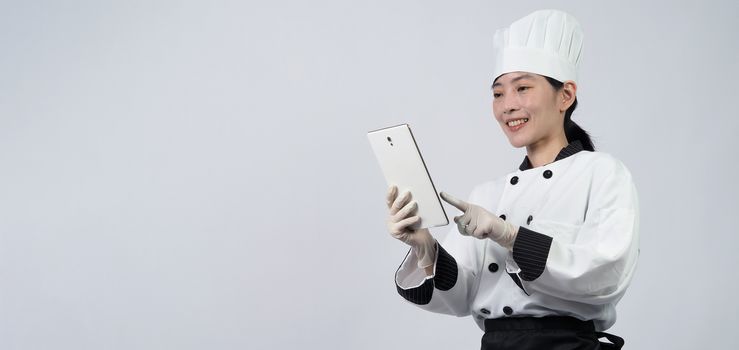 Middle aged of asian woman chef holding smartphone or digital tablet and received order from online shop or merchant application. she smiling in chef uniform and standing in studio with white color background.