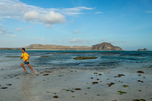 young man jogging on the beach in summer. Indonesian teenager in shorts and a yellow T-shirt running on the beach.