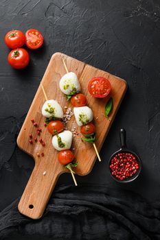 caprese salad skewer with tomato on sticks Italian traditional caprese salad ingredients. Mediterranean food. over black stone background overhead space for text vertical.