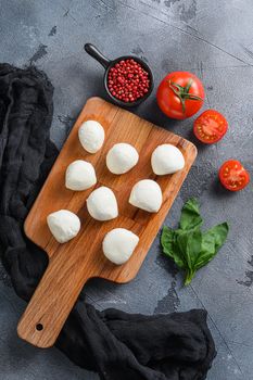 Buffalo Mozzarella cheese balls with fresh basil leaves and cherry tomatoes, the ingredients of the Italian Caprese salad, on a black cloth and grey concrete background vertical top view.