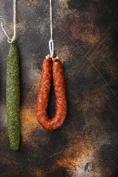 Dry cured chorizo and fuet salami sausages hanging on dark background, top view.