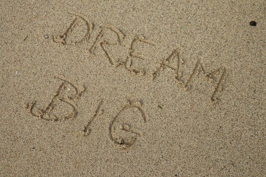 Handwritten DREAM BIG on a sandy sea beach on a summer sunny day. Disappearing dreams concept.
