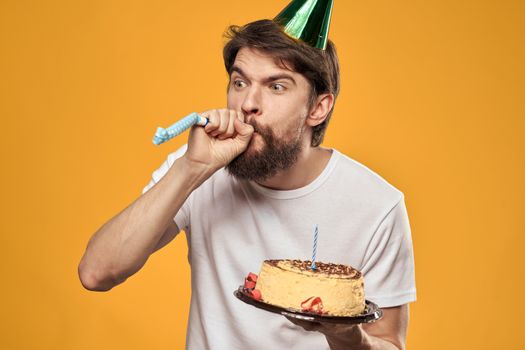 Handsome man with a beard and in a cap celebrating a birthday party yellow background. High quality photo