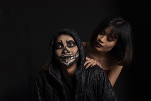 Southeast asian man with skull face makeup and woman on black background, portrait photography 