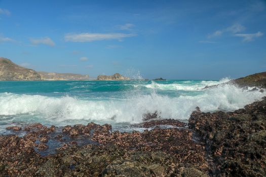 Waves splashing on a headland around Tanjung Aan beach. Dangerous phenomenon on a heavenly beach. Water is bubbled from the strength of the crushing waves. Beauty of the nature.