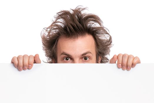 Crazy bearded Man with funny Haircut showing empty blank signboard with copy space. Guy with surprised eyes peeking out from behind big white banner, isolated on white background.