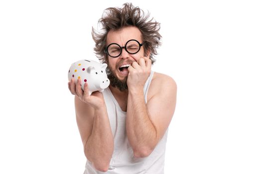 Crazy bearded Man with funny Haircut in eye Glasses holding Piggy Bank, isolated on white background. Saving Money concept. Male Screaming or Cry and about to break piggybank.