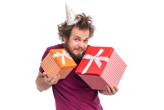 Crazy bearded Man with funny Haircut in birthday cap, isolated on white background. Happy guy holding gift boxes. Holidays concept.