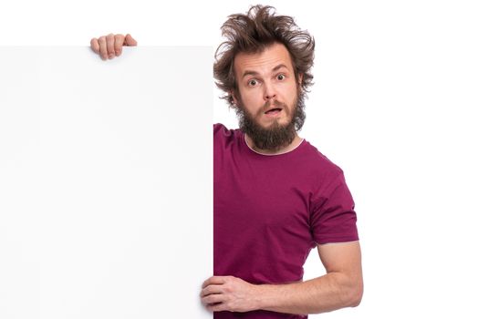 Crazy bearded Man with funny Haircut showing empty blank signboard with copy space. Guy with surprised eyes and mouth open peeking out from behind big white banner, isolated on white background.