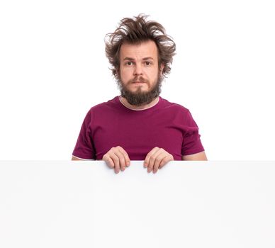 Crazy bearded modest and embarrassed Man with funny Haircut showing empty blank signboard with copy space. He is Shy and peeking out from behind big white banner, isolated on white background.