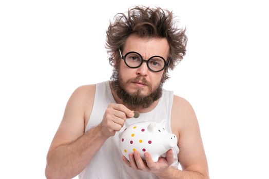 Crazy bearded Man with funny Haircut in eye Glasses holding Piggy Bank and coin, isolated on white background. Saving Money concept. Male putting coin in his piggybank.