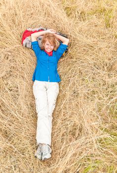 Young girl lying on grass in field. Beautiful woman in sport clothes resting with backpack under head. Happy smiling person relaxing in meadow. Outdoor activity and active people.