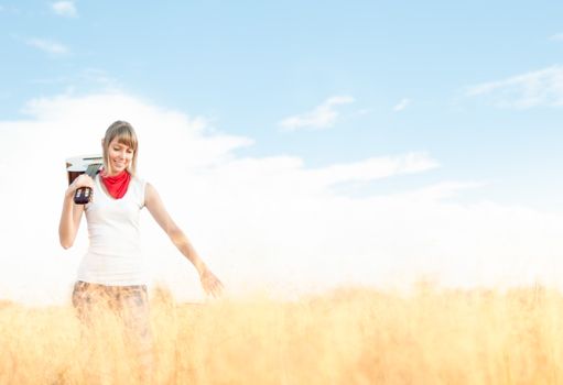 Beautiful woman standing on meadow with guitar and smiling. Young girl holding musical instrument. Yellow grass in foreground and clear blue sky in background. Active outdoor and leisure time.