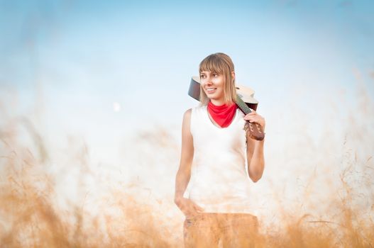 Beautiful woman standing on meadow with guitar and smiling. Young girl holding musical instrument. Yellow grass in foreground and clear blue sky in background. Active outdoor and leisure time.