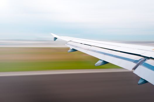 View of air plane wing during take off or landing. Motion blur of airport grounds and sky.