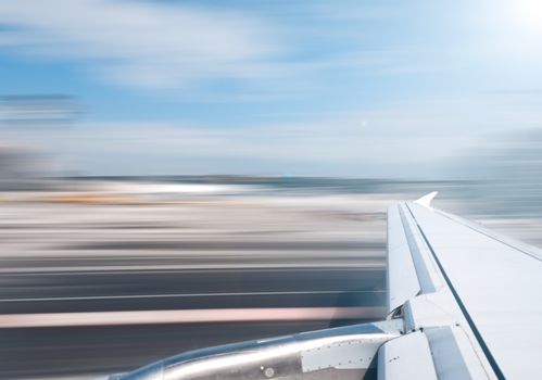 View of air plane wing during take off or landing. Motion blur of airport grounds and sky.