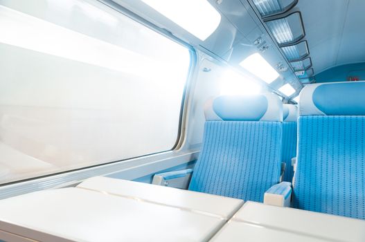 Inside cabin of modern express train. Nobody in blue chairs at window. Motion blur. Comfortable chairs and table in foreground, sun in background. Travel, France, Europe.