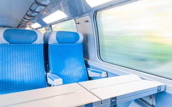 Inside cabin of modern express train. Nobody in blue chairs at window. Motion blur. Comfortable chairs and table in foreground, nature outside window. Travel, France, Europe.