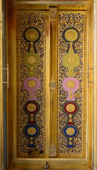 the wood carving door panels with painted royal insignias on a door panel, among flowery patterns, appear the first classes of each insignia category at Wat Ratchabophit, Bangkok, Thailand