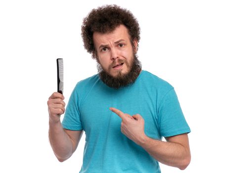 Crazy bearded Man with funny Curly Hair tries to comb his tangled and naughty hair with a small black hairbrush. Surprised face of guy who holds comb, isolated on white background.