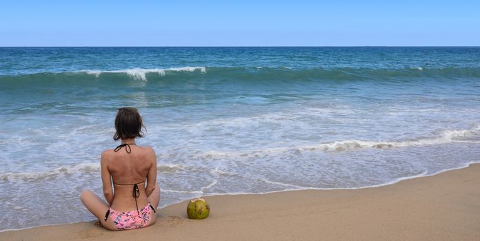 Sexy bikini body woman sitting on a beautiful beach and coconut on travel vacation. Banner crop for copy space.

