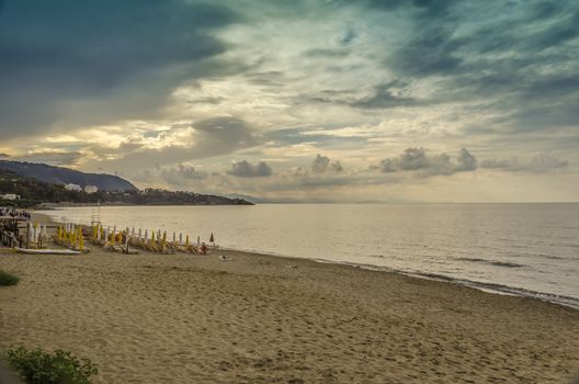beach with umbrellas and mountains on a sunset with clouds in the city of cefalu