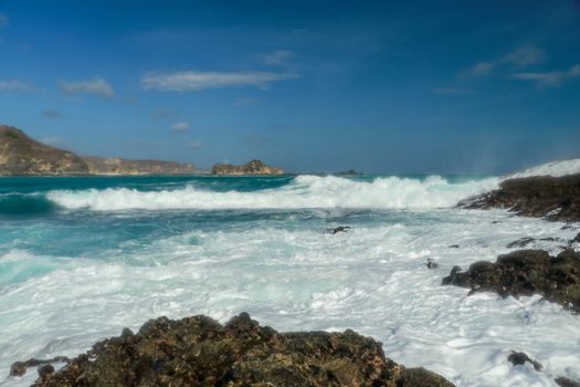 Waves splashing on sharp cliffs of Tanjung Aan beach. Dangerous phenomenon on a heavenly beach. Water is bubbled from the strength of the crushing waves. Beauty of the nature.