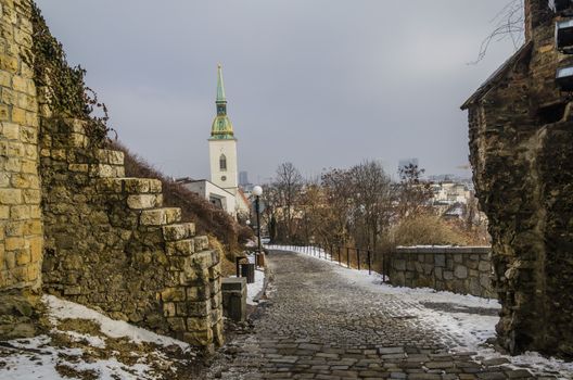 Old cobblestone road leading to Bratislava castle and to the background slovak church with its traditional dome after a snowfall