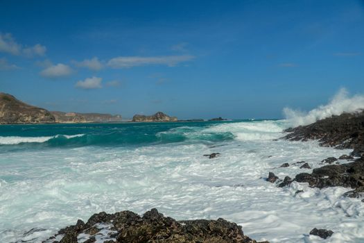 Waves splashing on sharp cliffs of Tanjung Aan beach. Dangerous phenomenon on a heavenly beach. Water is bubbled from the strength of the crushing waves. Beauty of the nature.