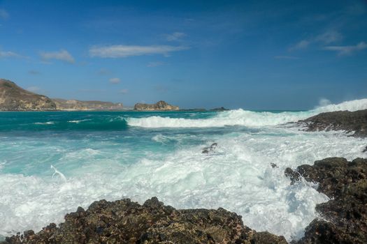 Waves splashing on sharp cliffs of Tanjung Aan beach. Dangerous phenomenon on a heavenly beach. Water is bubbled from the strength of the crushing waves. Beauty of the nature.