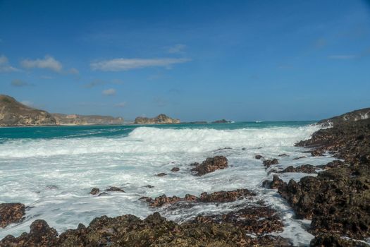 Waves splashing on sharp cliffs of Tanjung Aan beach. Dangerous phenomenon on a heavenly beach. Water is bubbled from the strength of the crushing waves. Beauty of the nature.