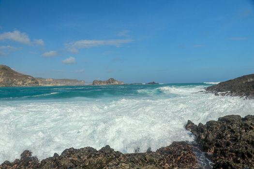 Waves splashing on sharp cliffs of Tanjung Aan beach. Dangerous phenomenon on a heavenly beach. Water is bubbled from the strength of the crushing waves. Beauty of the nature.