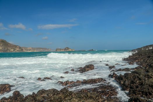 Waves splashing on sharp cliffs of Tanjung Aan beach. Dangerous phenomenon on a heavenly beach. Water is bubbled from the strength of the crushing waves. Beauty of the nature.