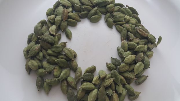 Closeup top view of dried green Elettaria cardamomum fruits with seeds, cardamom spice arranged in ring on a white background