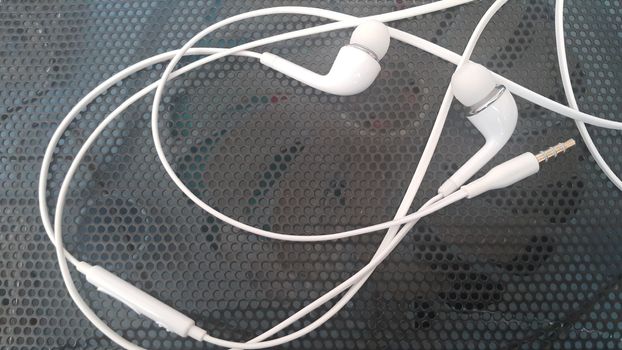 White headphones with headset lying on black background of metal gauze