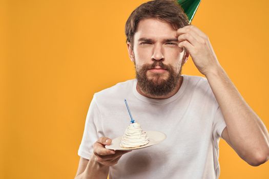 Handsome man with a beard and in a cap celebrating a birthday party yellow background. High quality photo