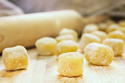 Raw gnocchi on  wooden board   , uncooked food with flour  , in the background a rolling pin