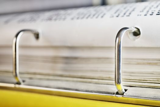 Open yellow binder close up , stack of white papers and bright metal rings , in the background black text out of focus