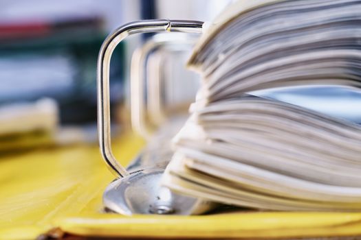 Open yellow binder close up , stack of white papers and bright metal rings , in the background office folders