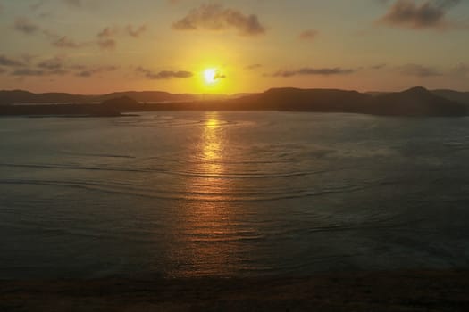 Sunrise view from rock at Tanjung Aan. Rising sun over Tanjung Aan Bay, Lombok, Indonesia. Reflection of the sun's rays on the sea surface. Sunset.