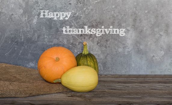 Happy Thanksgiving greeting text with colorful pumpkins over concrete background.