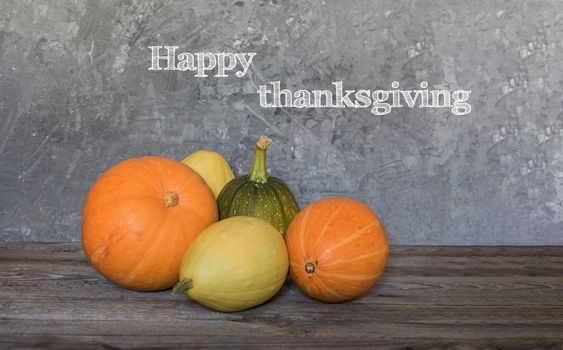 Happy Thanksgiving greeting text with colorful pumpkins over concrete background.