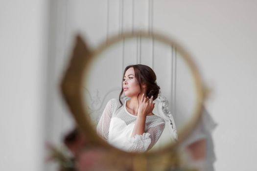 Portrait of the bride in a white wedding dress in a beautiful round mirror.