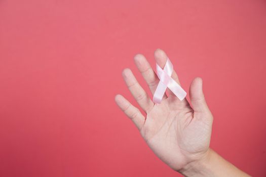 Pink ribbon on a woman hands on pink background. Breast cancer, healthcare and medicine concept, symbolic tape