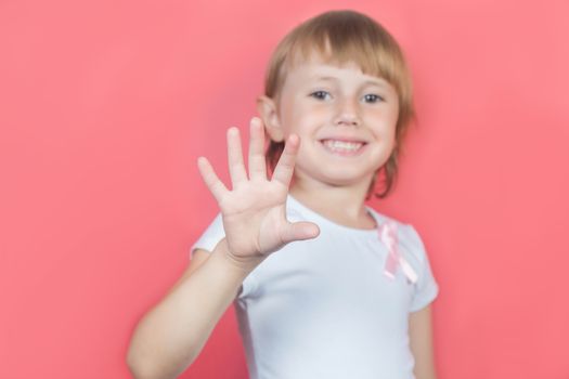 Little girl showing five fingers sign wearing white t-shirt and with pink breast cancer awareness ribbon