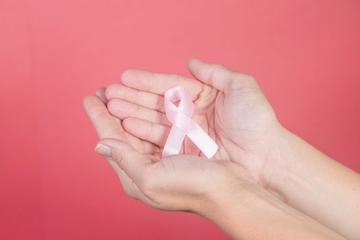 Pink ribbon on a woman hands on pink background. Breast cancer, healthcare and medicine concept, symbolic tape